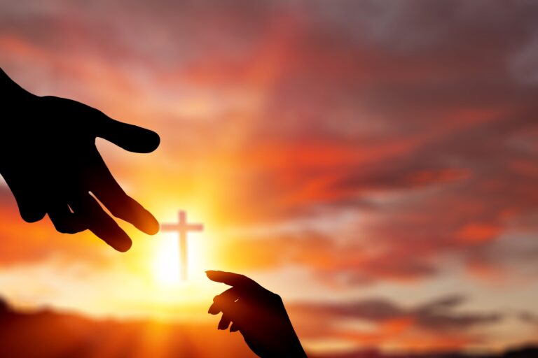 A hand reaching down to take another hand with a cross in the background.